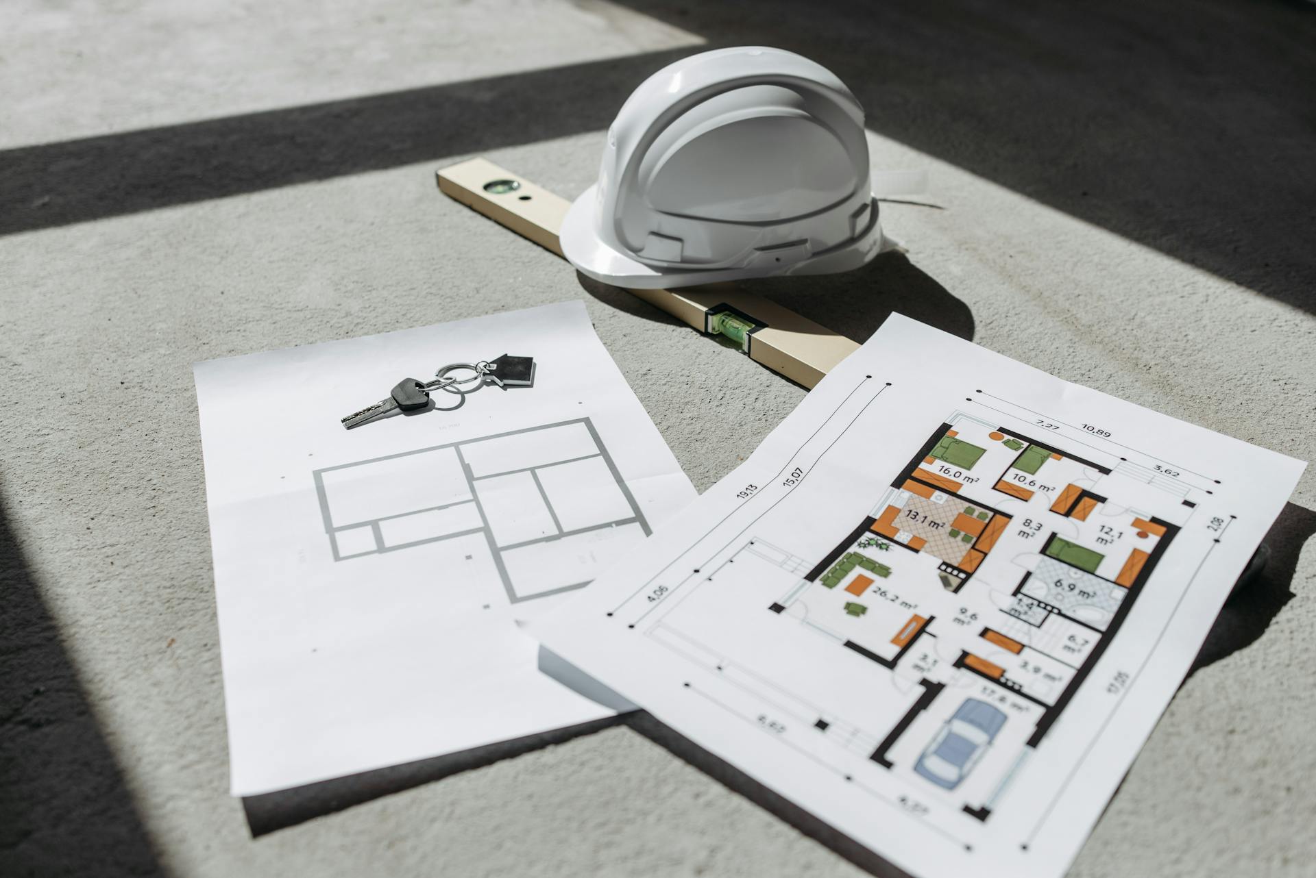 Architectural floor plan, hard hat and keys laid on a concrete floor