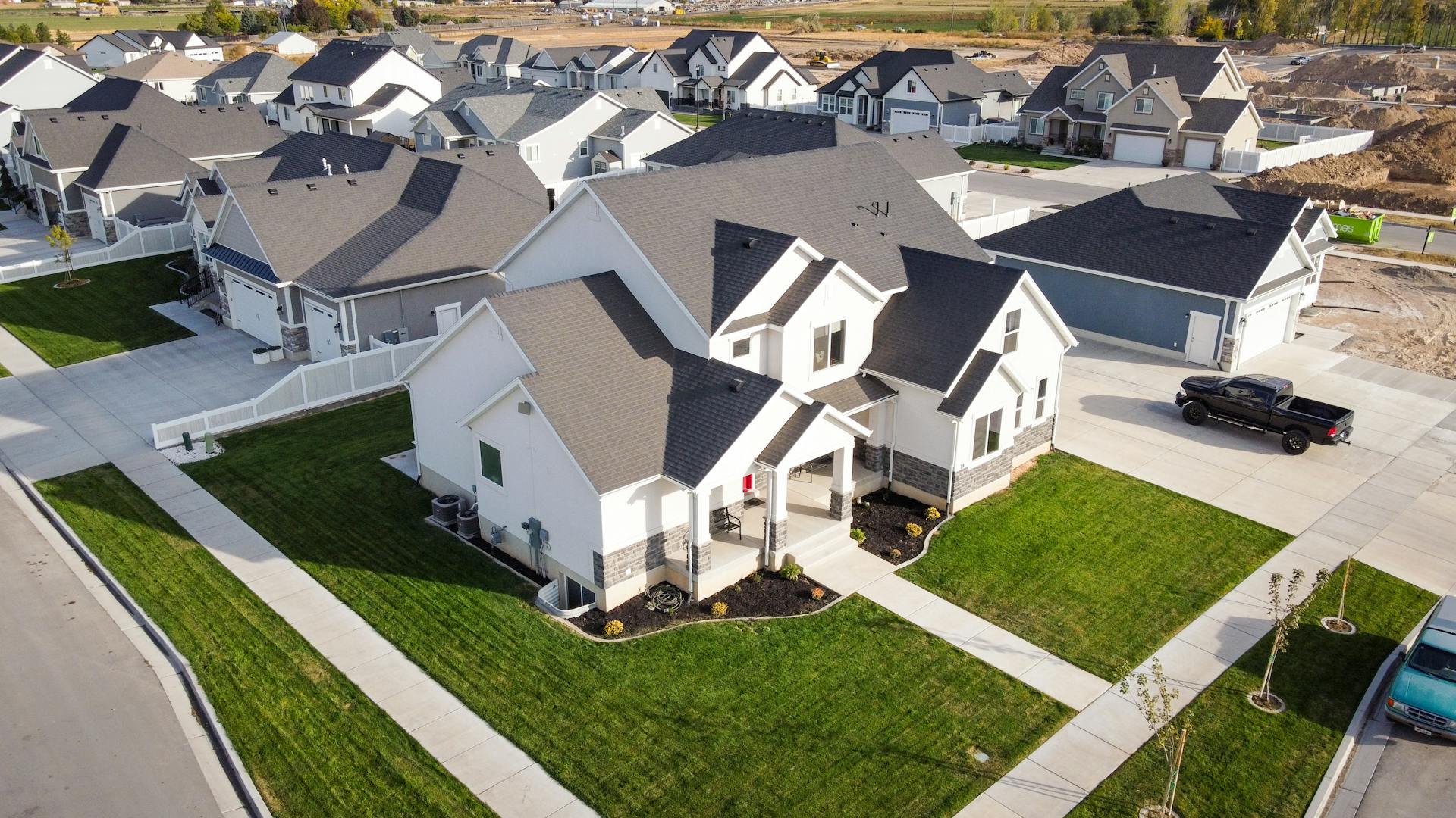 Aerial view of a new suburban estate with white detached houses, dark roofs, neat lawns and a wide cul-de-sac.